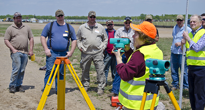 An instructor shows a group of students how to use surveying equipment outside.