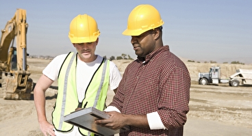Two workers looking at a clipboard at a construction site