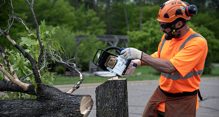 A person in safety gear demonstrates how to use a chainsaw.