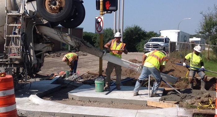 Workers wearing safety vests guide concrete out of a truck to create a curb cut.