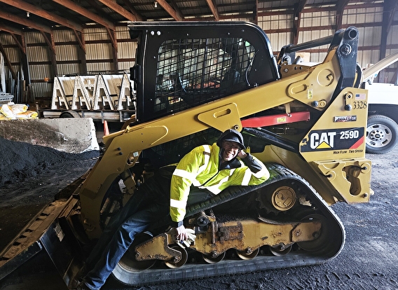 A person lays across the track of a piece of construction equipment and smiles at the camera.