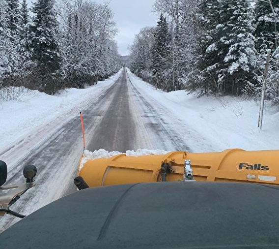 View over the hood of a snowplow, looking out at the plow and a partially snow-covered road