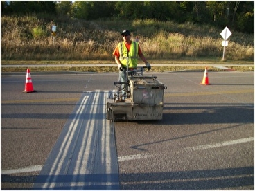 Scott County worker installing a thermoplastic coating across a road