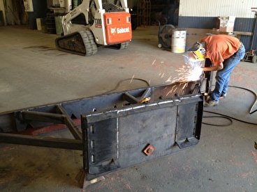 Worker welding the skid loader screed attachment