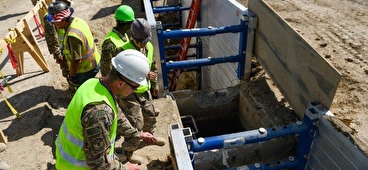 Workers in safety helmets and vests work on an excavation project.