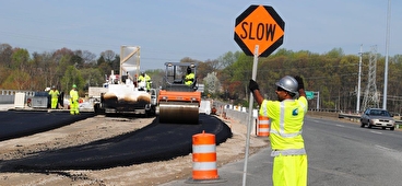 A person wearing a safety vest and helmet holds an orange SLOW sign in a work zone.